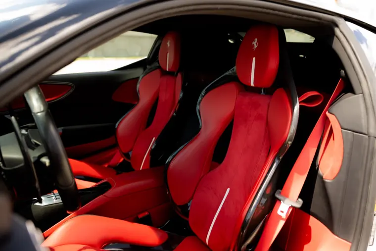 Red leather and Alcantara seats in the Ferrari SF90 rental, prancing horse headrests, carbon-shell seat backs and red belts, shot through the open driver door